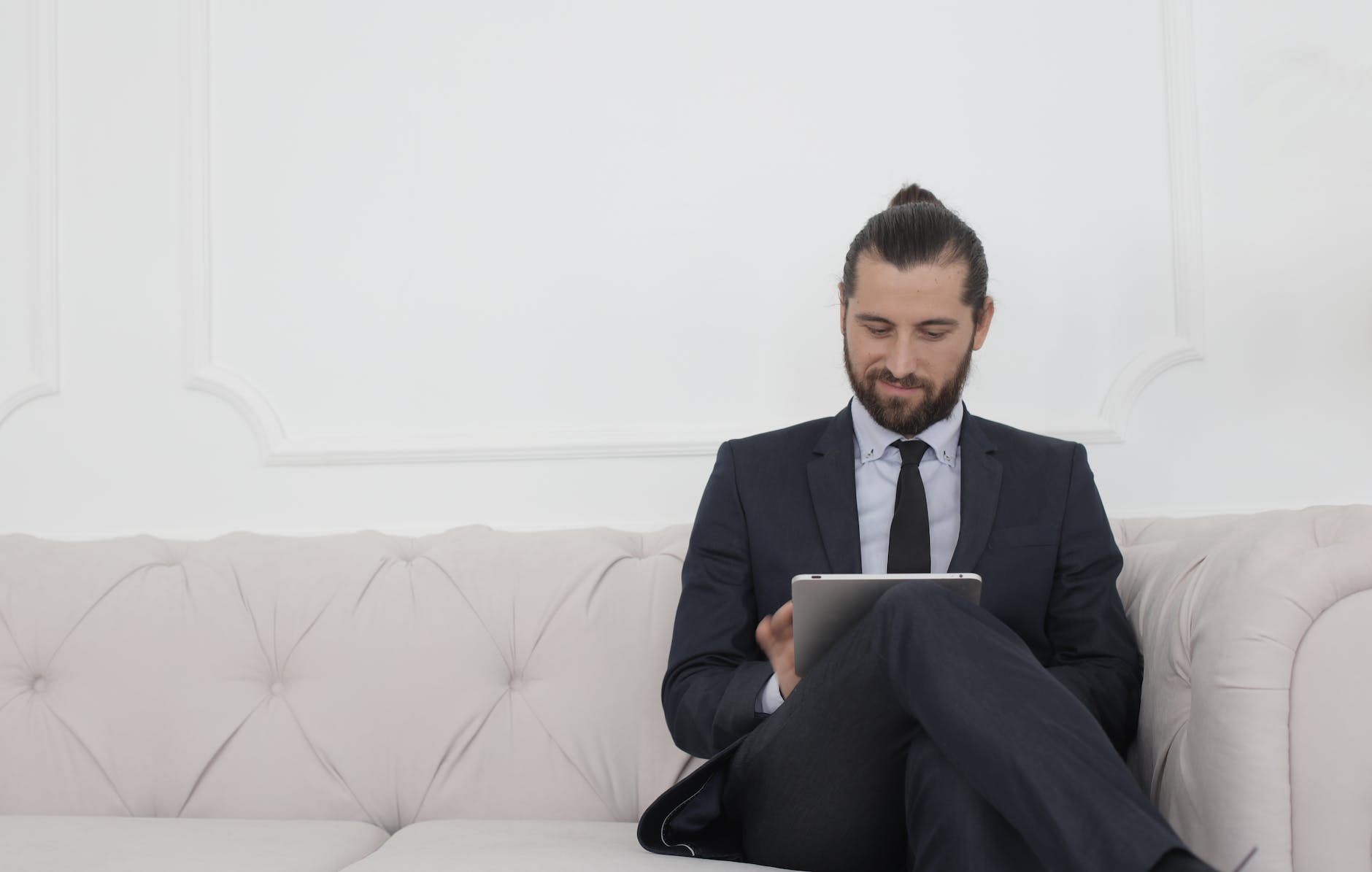 beard man in black suit sitting on white couch