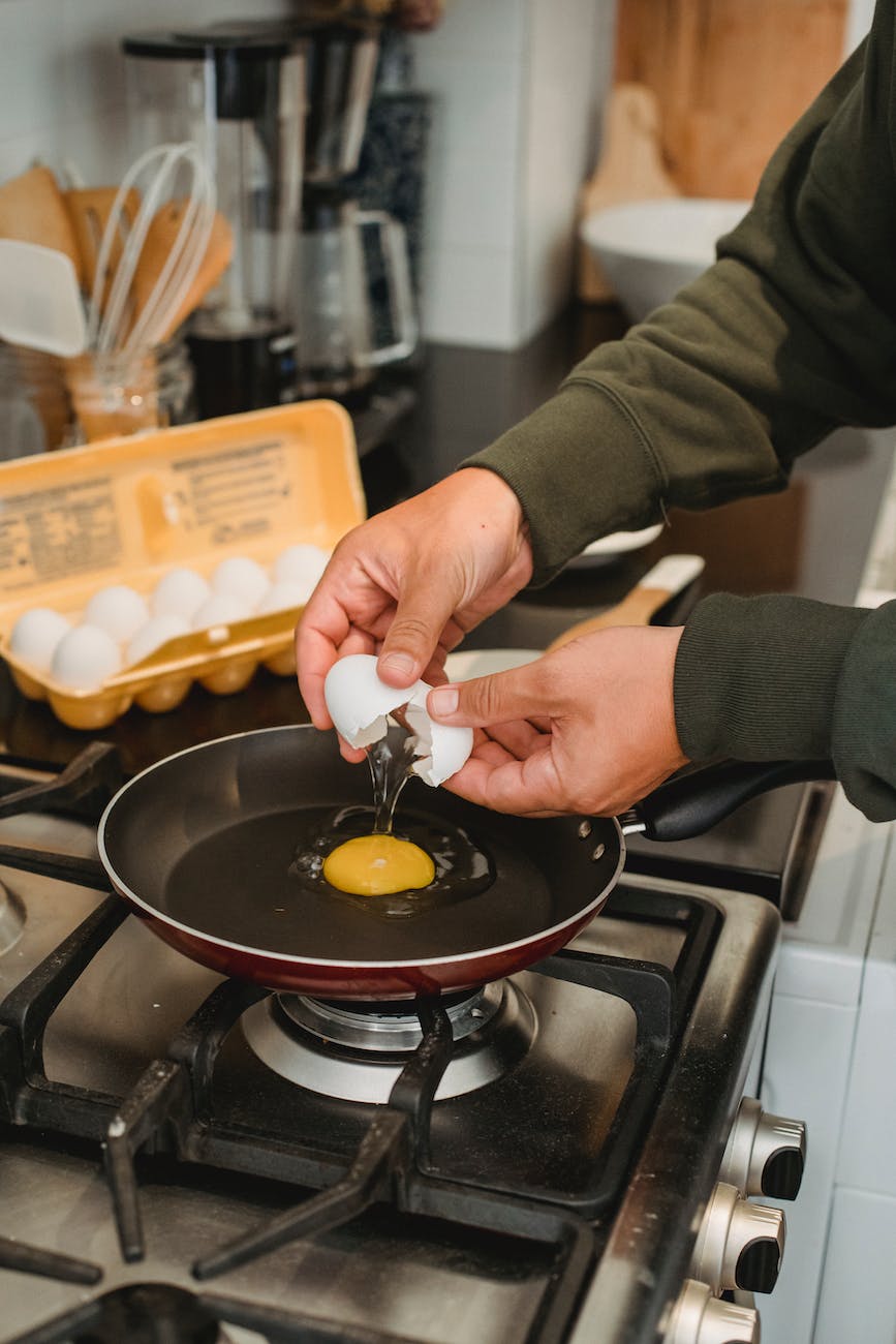 man breaking egg into pan in kitchen