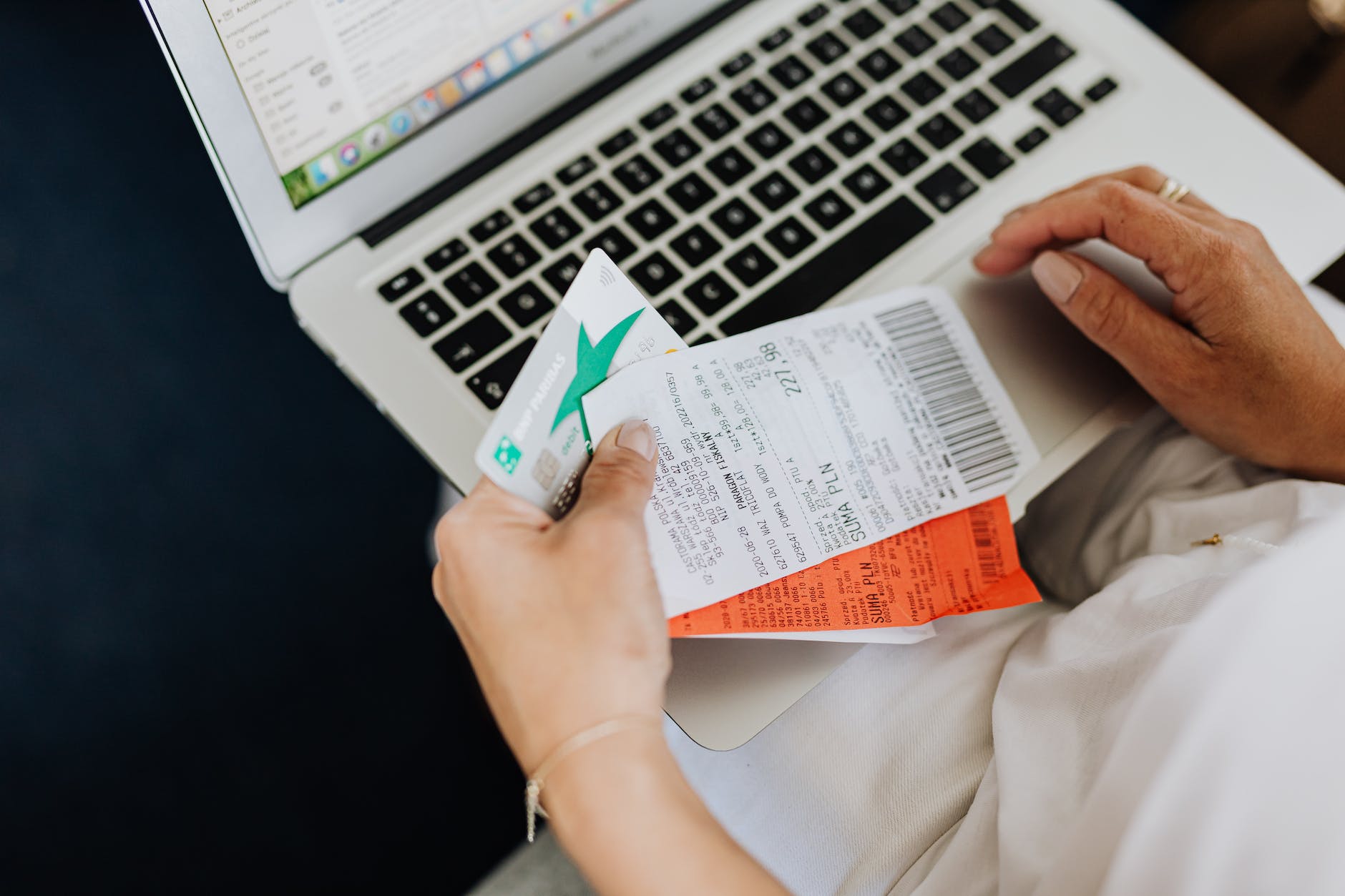 person using a computer and holding a credit card and receipts