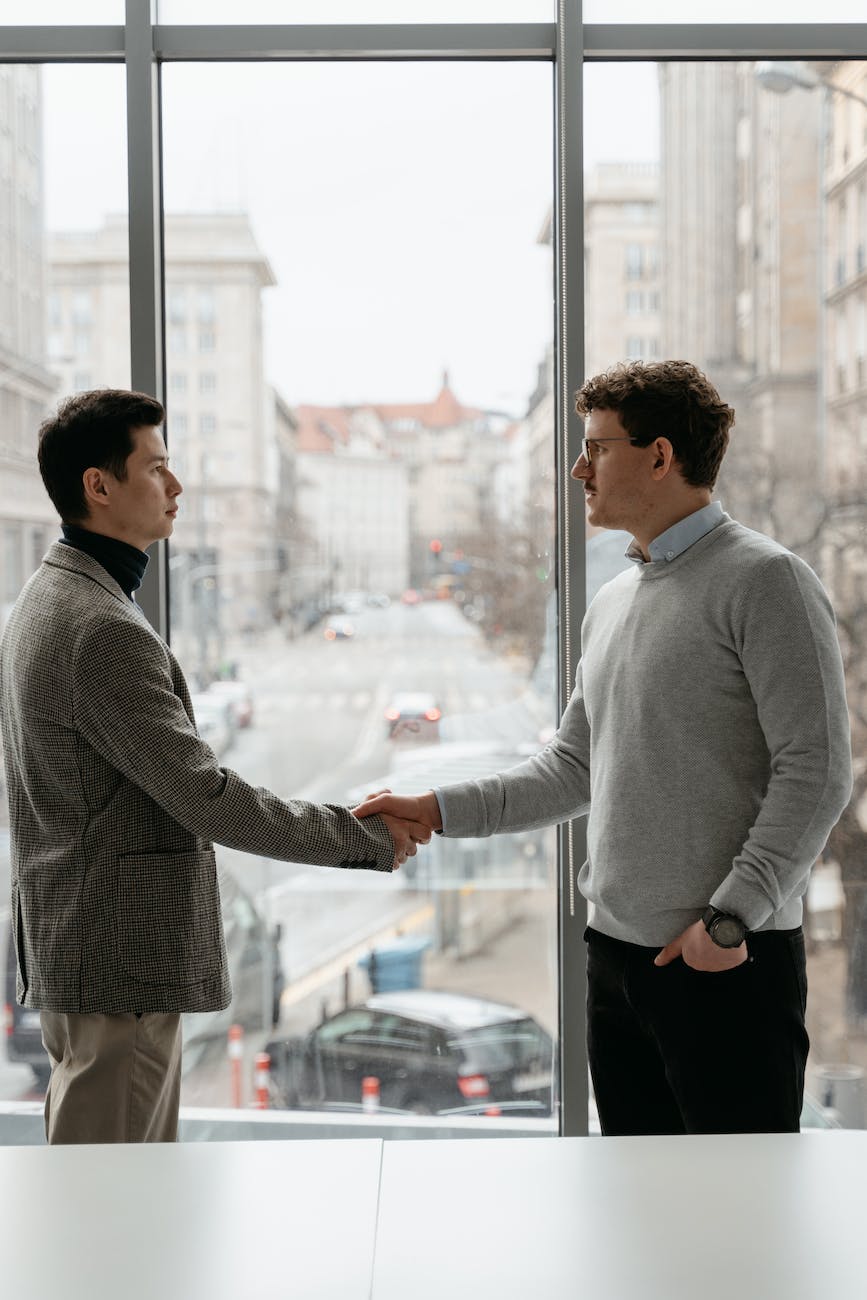 men in gray suit and sweater standing near the glass window while having a deal