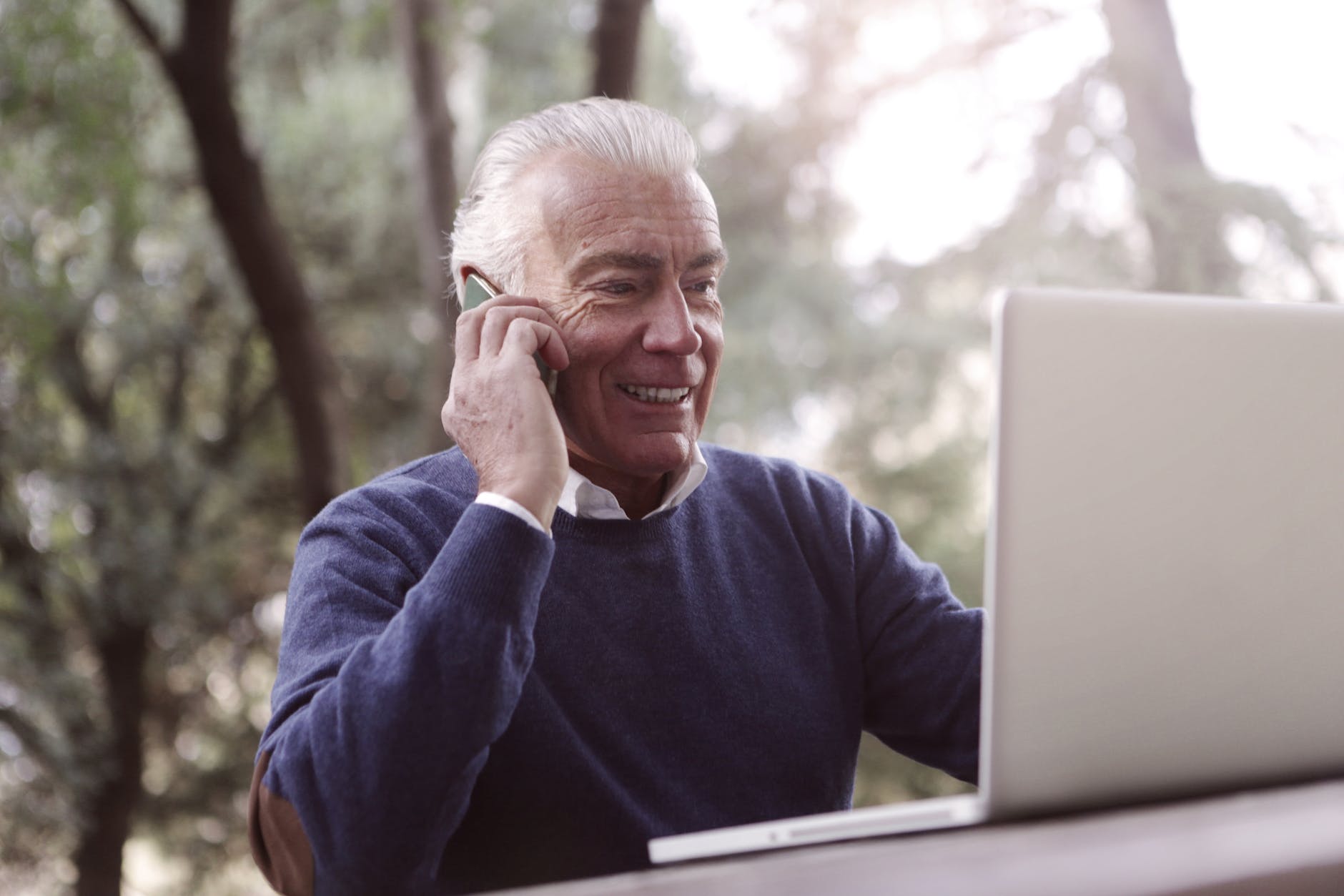 adult man wearing blue sweater using cellphone and laptop