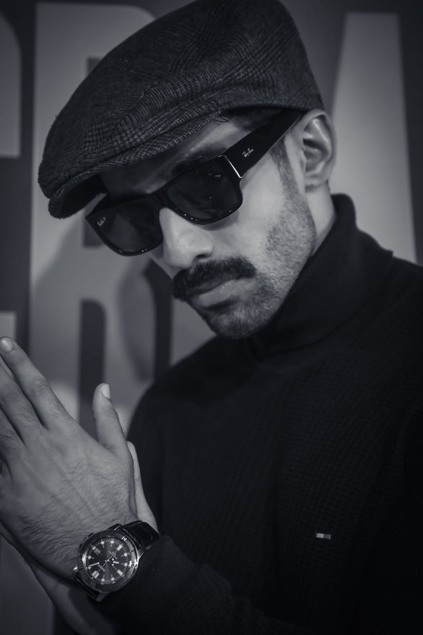 black and white photograph of a man wearing a flat cap sunglasses and a wristwatch