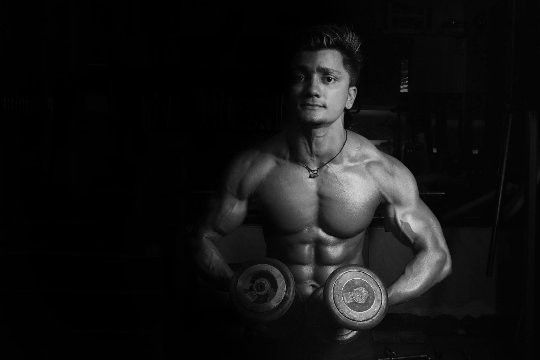 grayscale photo of a man holding pair of dumbbells