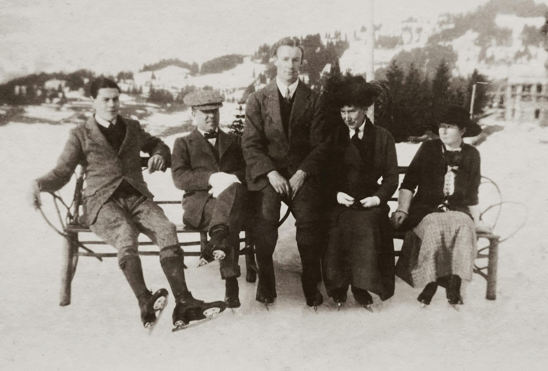 grayscale photo of people sitting on bench on a snow covered land